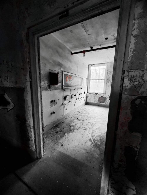 A dimly lit, abandoned room with peeling walls and a window, featuring a message on the wall that reads "DIE."
