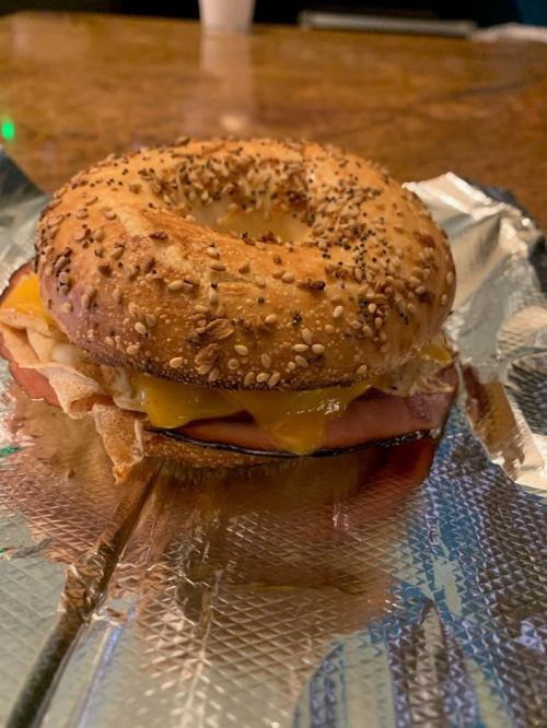 A toasted sesame bagel sandwich with cheese, ham, and egg, served on foil.