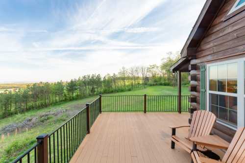 A wooden deck with two chairs overlooks a lush green landscape and blue sky.