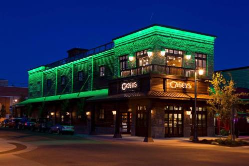 A brick restaurant building with green lighting at night, featuring large windows and a welcoming entrance.