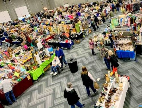 A bustling indoor market with numerous vendors and shoppers browsing various goods and crafts.