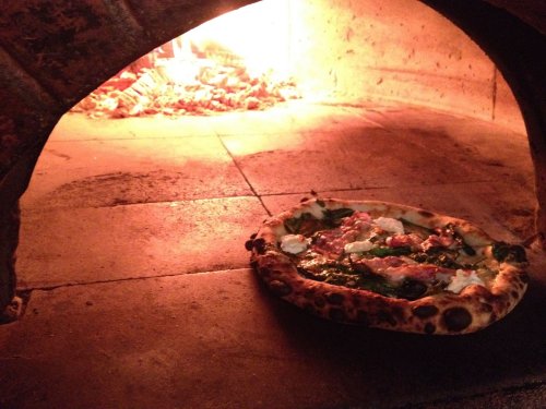 A freshly baked pizza with toppings, resting in a wood-fired oven with glowing embers in the background.