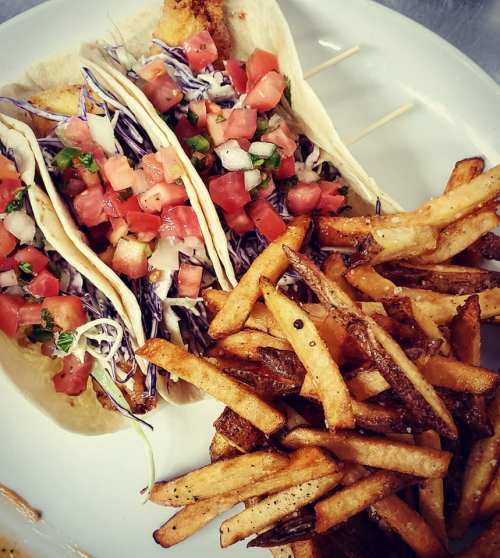 Two tacos filled with cabbage, tomatoes, and cilantro, served with a side of crispy French fries.
