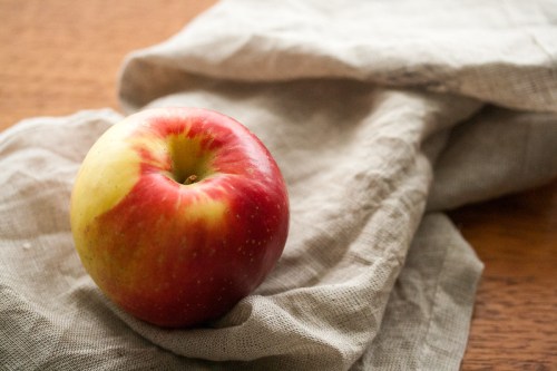 A red and yellow apple resting on a crumpled beige cloth on a wooden surface.