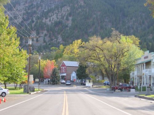 A quiet street in a small town, lined with trees and buildings, set against a backdrop of mountains.