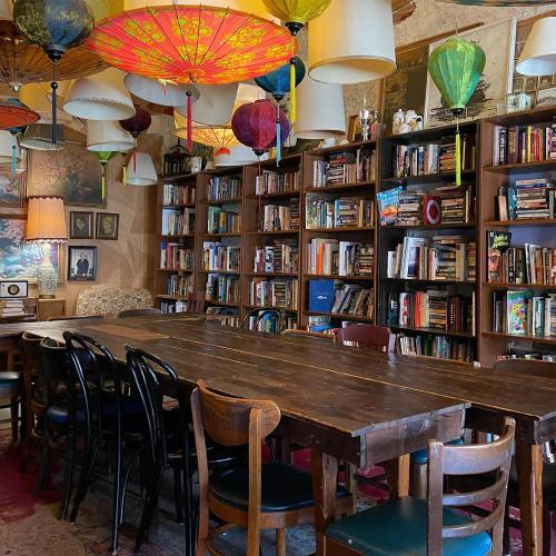 Cozy library with colorful lanterns, wooden bookshelves filled with books, and a large table surrounded by chairs.