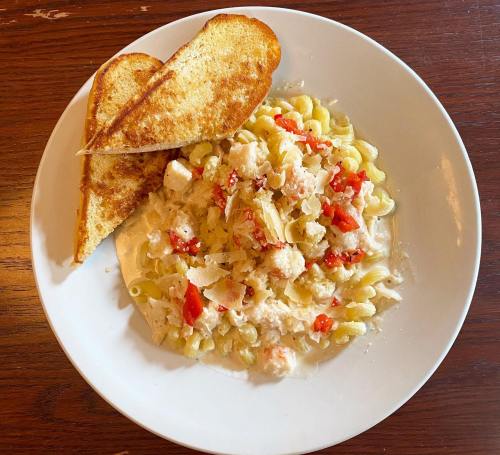 A plate of creamy pasta with lobster and red peppers, served with two slices of toasted bread.