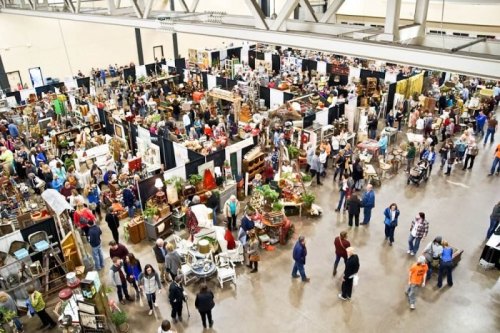 A bustling indoor market filled with vendors and shoppers exploring various antiques and crafts.