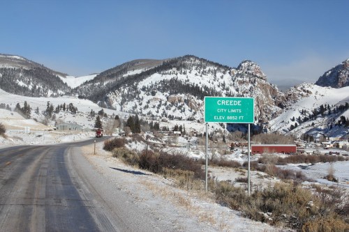 Sign marking the city limits of Creede, Colorado, with snowy mountains in the background and a clear blue sky.