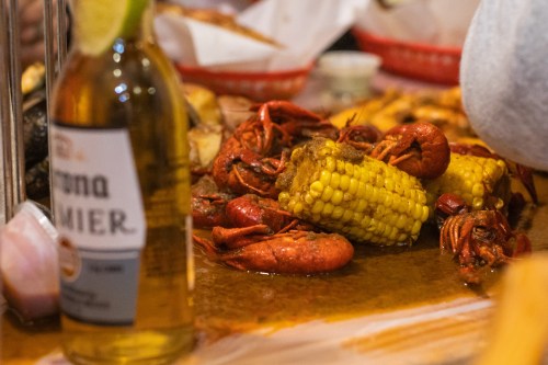 A close-up of a seafood feast featuring crawfish, corn, and a bottle of beer on a table.