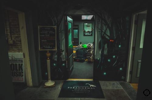 A dimly lit hallway with a mysterious entrance, featuring eerie wall art and a sign for a paranormal investigation center.