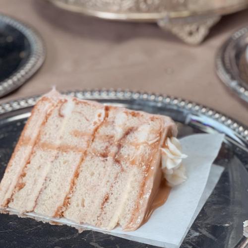 A slice of cake with a caramel drizzle and whipped cream, placed on a decorative silver platter.