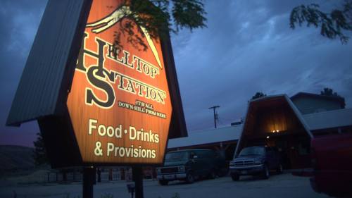 Sign for Hilltop Station, featuring "Food, Drinks & Provisions," with a rustic building in the background under a cloudy sky.