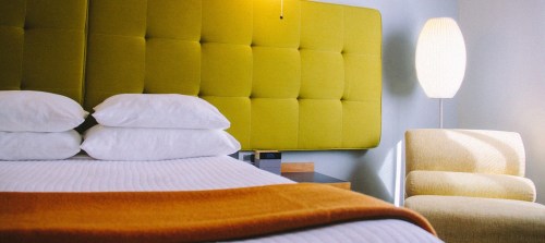 A modern hotel room featuring a green upholstered headboard, a cozy bed with white pillows, and a stylish armchair.