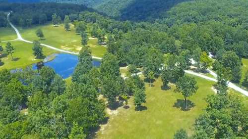 Aerial view of a lush green landscape with trees, a small pond, and winding paths through the countryside.