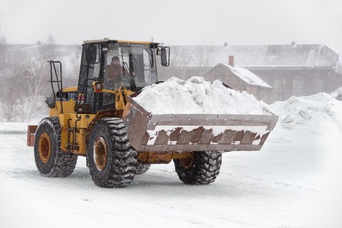 A yellow snowplow truck clears snow in a snowy landscape during a winter storm.