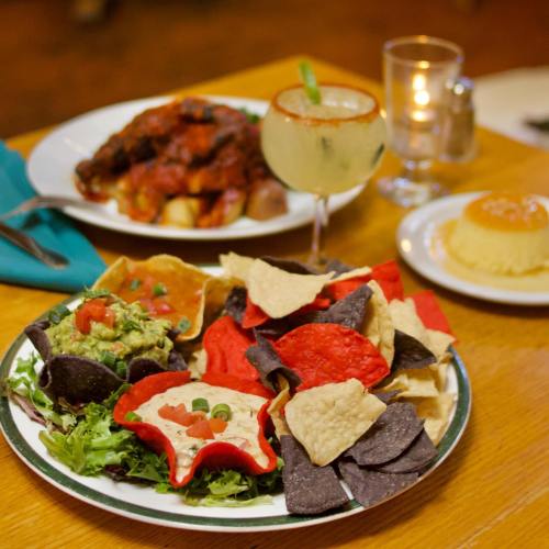 A colorful platter of nachos with guacamole, a margarita, and a dessert on a wooden table.
