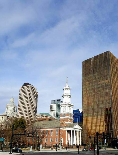 A historic building with a clock tower in front of modern skyscrapers under a partly cloudy sky.
