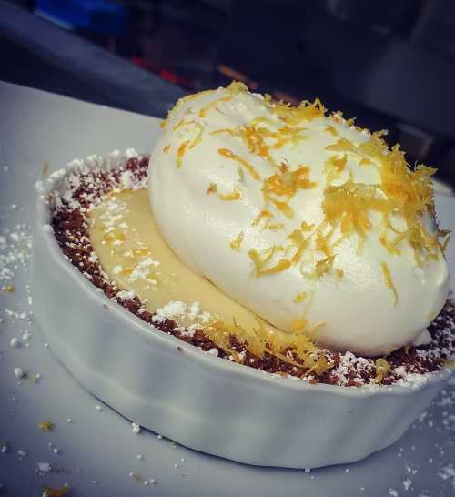 A dessert in a white dish featuring a creamy filling topped with fluffy whipped cream and yellow citrus zest.