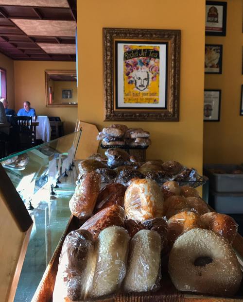 A display of assorted wrapped pastries and bagels in a café, with a colorful framed artwork on the wall.
