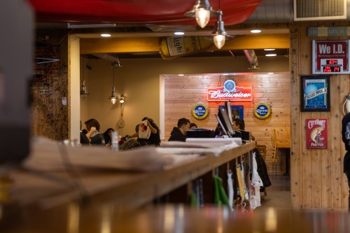 A cozy bar interior with wooden decor, featuring a Budweiser sign and patrons enjoying their time.