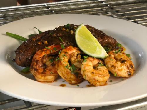 A plate featuring grilled steak and shrimp, garnished with lime and herbs, served on a bed of green beans.