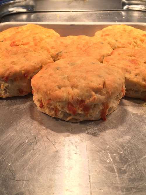 Freshly baked biscuits with a golden crust, arranged on a metal tray.