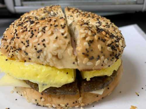 A toasted bagel with sesame and poppy seeds, filled with cheese, egg, and a sausage patty, cut in half.