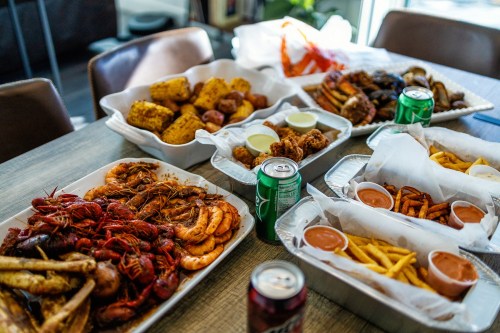 A spread of seafood and fried dishes, including shrimp, crawfish, fries, and dipping sauces, on a table.
