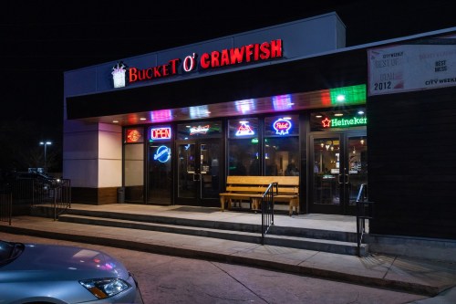 Exterior of "Bucket O' Crawfish" restaurant at night, featuring neon signs and a welcoming open door.
