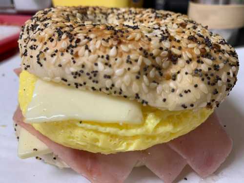 A toasted bagel topped with layers of egg, cheese, and ham, sprinkled with sesame and poppy seeds.