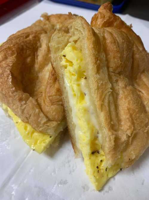 A close-up of a croissant sandwich filled with fluffy scrambled eggs and creamy filling, resting on a white surface.