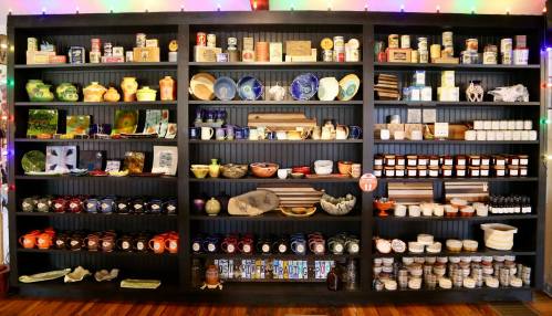 A colorful display of various jars, bowls, and decorative items arranged on black shelves with festive lights in the background.