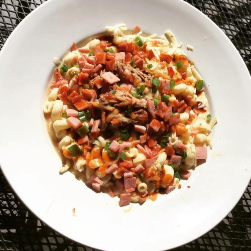 A plate of pasta topped with diced ham, green onions, and a drizzle of sauce, served on a textured black surface.
