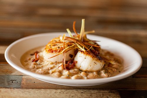A plate of seared scallops on a creamy bean puree, garnished with crispy onions and bacon bits.