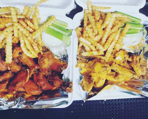 Two takeout containers with crispy fries, celery sticks, and chicken wings in different sauces.