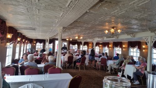 A spacious dining room with large windows, filled with seated guests and elegant decor, enjoying a gathering or event.