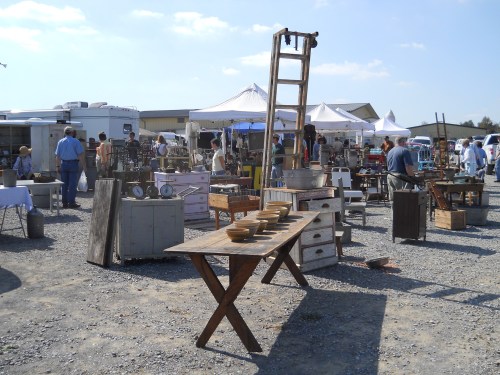 A bustling outdoor market with various vintage items, tables, and tents under a clear blue sky.