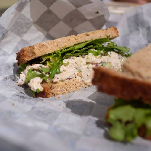 A sandwich with chicken salad and fresh greens on whole grain bread, wrapped in paper.