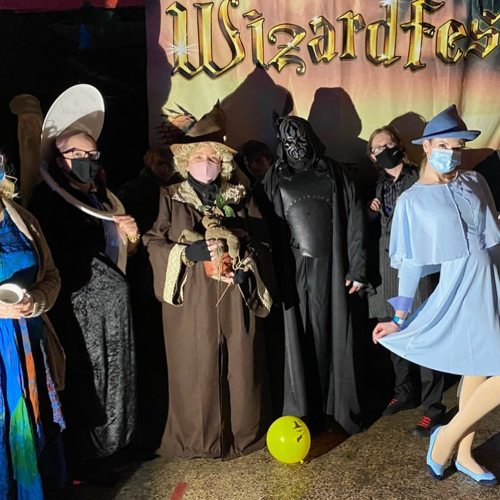 A group of people in costumes at Wizardfest, featuring witches, a dark figure, and a character in a blue dress.
