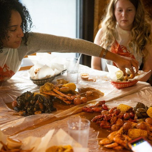 Two women enjoy a seafood feast at a table covered with food, including shrimp, crab, and corn.
