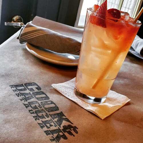 A refreshing drink with strawberries sits on a table with a napkin and a plate in a restaurant setting.