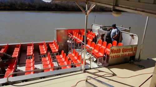 A boat with bright orange seats along the river, featuring a sign for "Moab Queen II."
