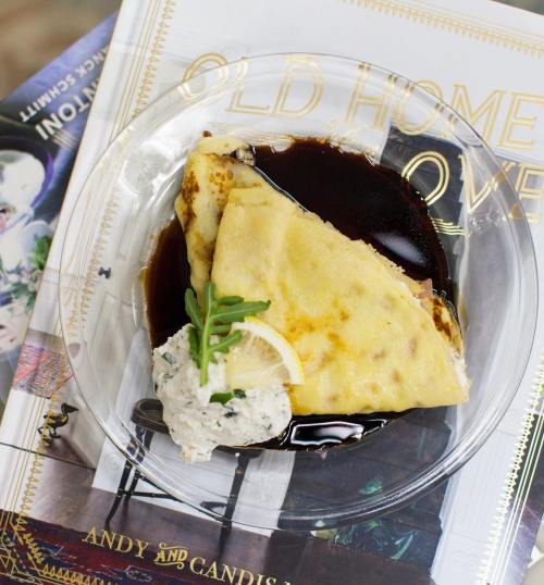A plate with a folded crepe drizzled in dark sauce, accompanied by a dollop of creamy filling and garnished with herbs.