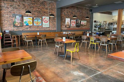 A spacious restaurant with wooden tables, colorful chairs, and brick walls adorned with artwork.