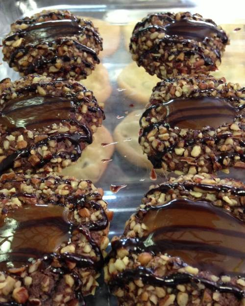 A tray of cookies topped with chocolate and chopped nuts, with some plain cookies in the background.
