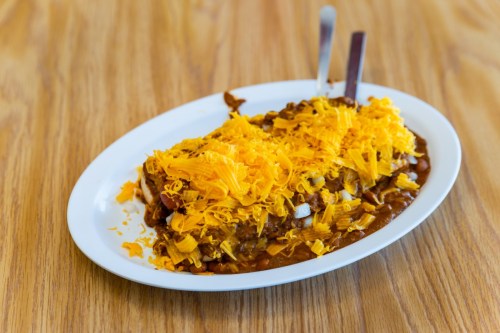 A plate of chili topped with shredded cheese, served on a wooden table.