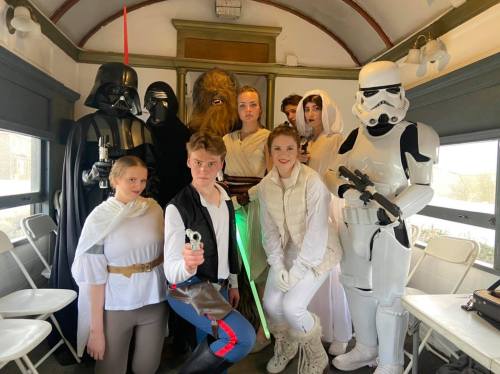 A group of people dressed as Star Wars characters, including Darth Vader, Chewbacca, and a Stormtrooper, posing together.