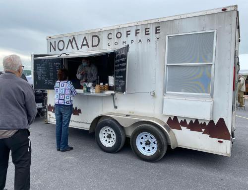A coffee truck with a menu displayed, customers waiting in line at an outdoor location.