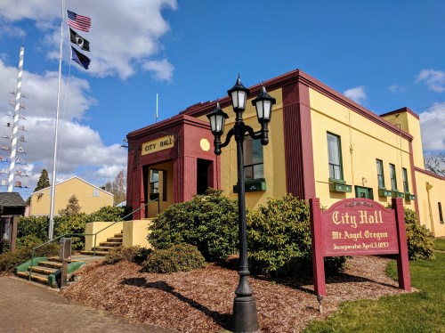 City Hall building in Mt. Angel, Oregon, with flags and a sign indicating its incorporation date.